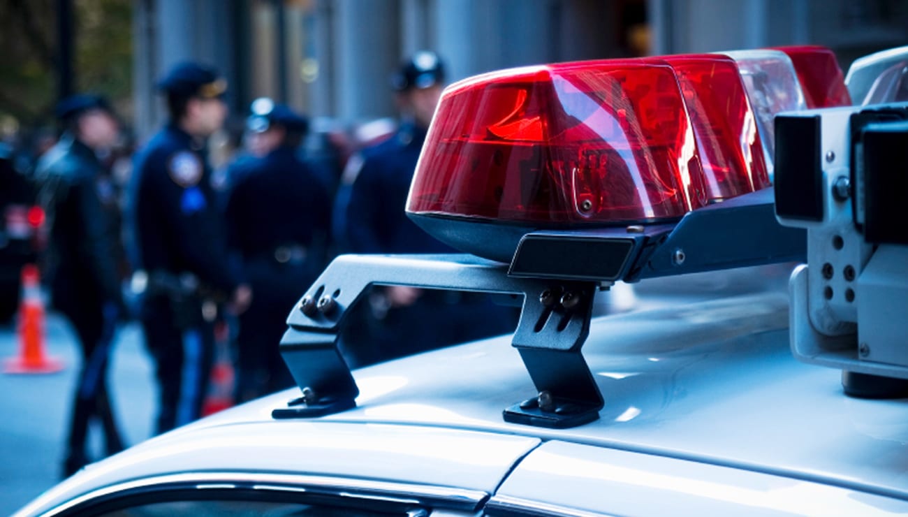 Police vehicle emergency lights with officers in the background, representing collaboration with law enforcement on unsolved cases