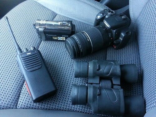 Professional investigation equipment including a camera, two-way radio, and binoculars used in missing persons fieldwork