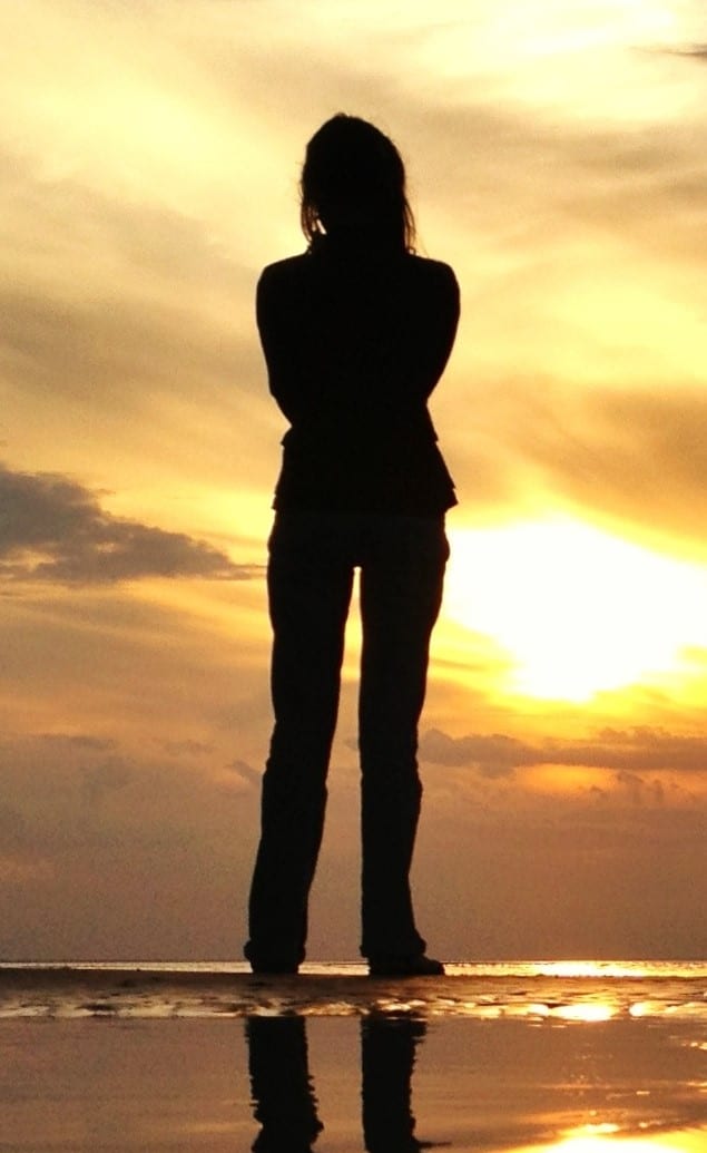A person stands alone at sunset, looking toward the horizon with hope for a missing loved one's return